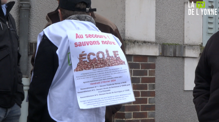 photo d'une femme portant une pancarte sur le dos "au secours, sauvons notre école !"